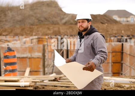 Male engineer holding drawing plan of hause at construction site. Stock Photo