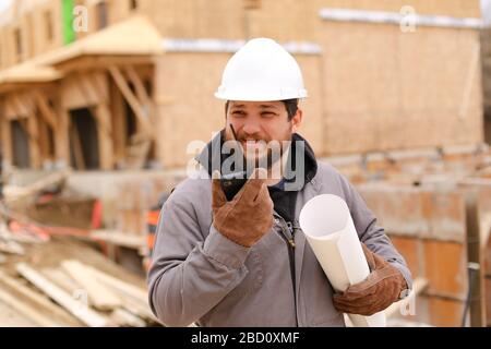 Foreman speaking by walkie talkie and holding drawing plan at construction site. Stock Photo