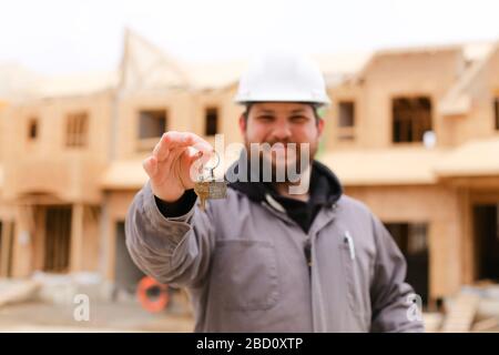 Focus on apartment keys, foreman giving and wearing hardhat. Stock Photo