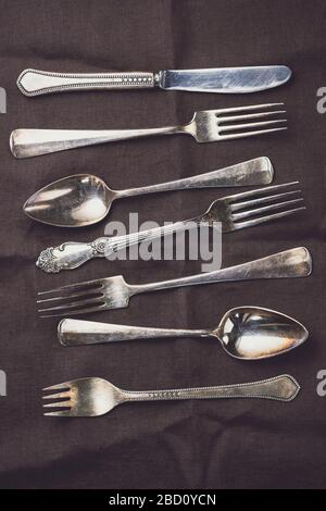 Metal vintage cutlery on a dark linen napkin in a row. Flat lay, top view. Stock Photo