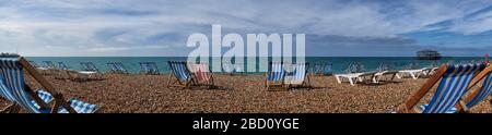 Panoramic view of empty deckchairs and sun loungers facing out to sea on Brighton pebble beach Stock Photo