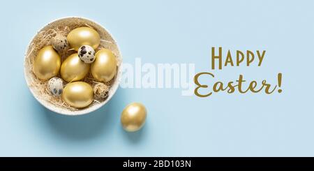 Easter banner with golden chicken eggs in bowl on blue background. Greeting card with text - Happy Easter. View from above. Stock Photo