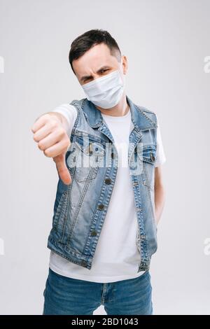 Portrait of young male wearing medical mask is showing thumbs-up gesture. Stock Photo
