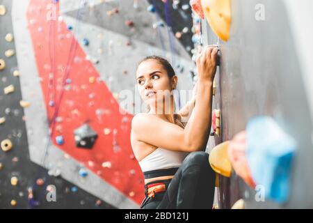 Sportswoman climber moving up on steep rock, climbing on artificial wall indoors. Extreme sports and bouldering concept Stock Photo