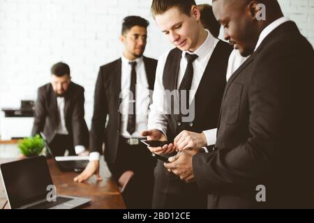 Dialogue of two men with with smartphones young businessmen in suits working and communicating together in an office. Corporate businessteam and Stock Photo