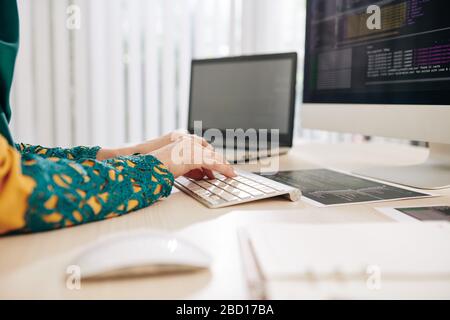 Hands of female coder sitting at her office desk and writing program Stock Photo
