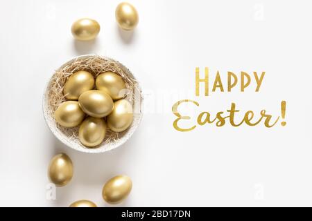 Easter greeting card with golden chicken eggs in bowl on white background. Text - Happy Easter. View from above. Stock Photo