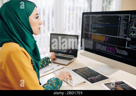 Young muslim coder using computer and laptop when testing new program whe wrote Stock Photo
