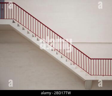 A View of stairs with red metal railings against a flat wall. Stock Photo