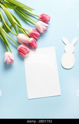 Bouquet pink tulips, easter bunny and blank for cheers on blue. Spring. Happy Easter holiday. Greeting card. Vertical. Top view. Stock Photo