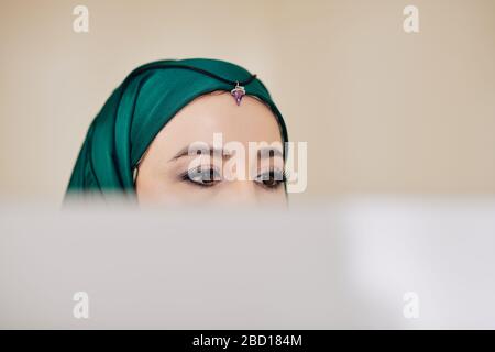 Muslim beautiful young woman in green hijab reading information on screen of computer Stock Photo