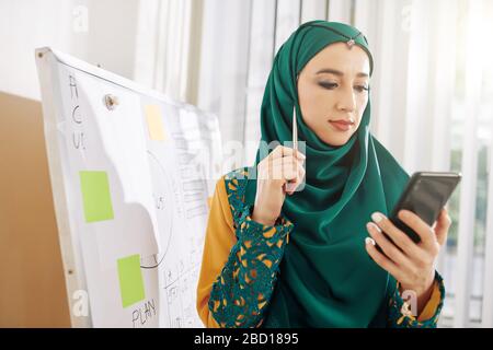 Portrait of young muslim businesswoman in traditional clothes reading article on smartphone screen Stock Photo