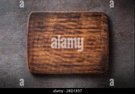 Top view of dark brown empty rustic wooden rectangular cutting board with rounded edges on a black metalic background. Stock Photo