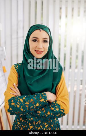 Portrait of smiling confident businessowoman in traditional muslim dress crossing arms and looking at camera Stock Photo