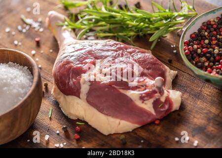 Close-up view of a raw unskinned duck leg with pepper, rosemary and salt on a dark wooden background. Stock Photo