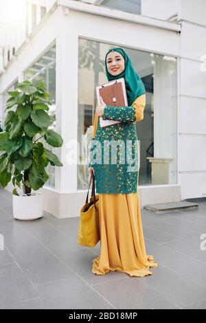 Happy smiling muslim female student with clipboard and tablet computer standing outdoors Stock Photo