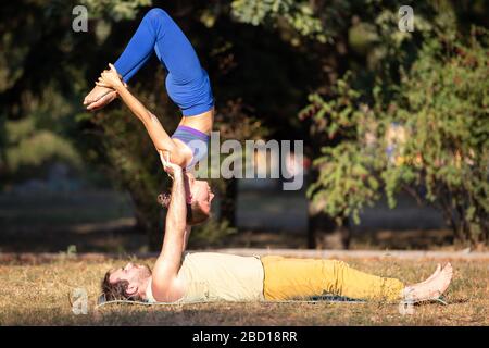 Young couple doing acroyoga exercises in park. Man holding woman on hands in acro yoga poses Stock Photo