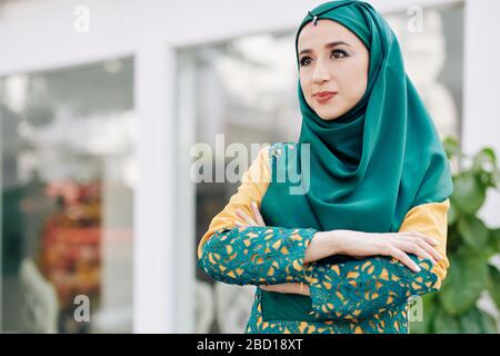 Confident determined young muslim woman in hijab folding arms and looking in front of her Stock Photo