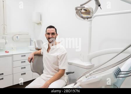 Portrait of a bearded dentist smiling at camera sitting on dentist chair. Stock Photo