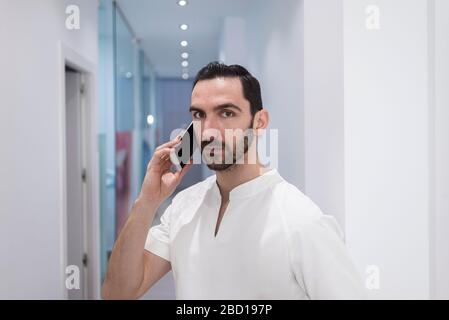 Doctor young man, medical professional happy talking using a smartphone mobile phone at hospital Stock Photo