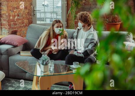 Woman and man, couple in protective masks and gloves isolated at home with coronavirus respiratory symptoms such as fever, headache, cough. Healthcare, medicine, quarantine, treatment concept.