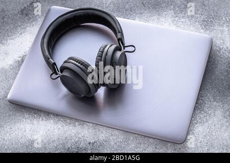 Black portable headphones on a purple metal notebook on grunge gray background. Closed laptop with earphones on grey backdrop Stock Photo