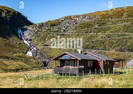 Norwegian traditional rural village black house with solar panels on serpentine mountain road on hill, waterfall distance view. Autumn drive scandinav Stock Photo