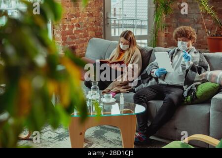 Woman and man, couple in protective masks and gloves isolated at home with coronavirus respiratory symptoms such as fever, headache, cough. Healthcare, medicine, quarantine, treatment concept.