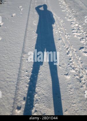 Silhouette of a active man taking his hand on the head while standing on an earth road covered with fresh snow Stock Photo