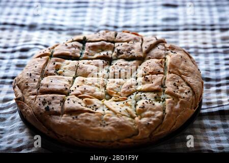 Healthy greek food concept. Whole spinach pie with sesame seeds or greek spanakopita with phyllo on kitchen table background. Stock Photo