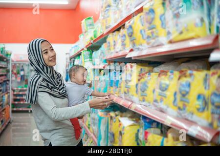 muslim asian mother buying baby product while carrying her daughter Stock Photo