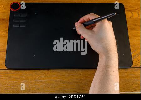 Isolated male hand on oak desk operating pen tablet (design concept) Stock Photo