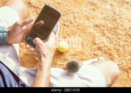 High angle shot of young tennis player taking rest after training and busy in using mobile phone - fitness, Sport and recreation concept Stock Photo