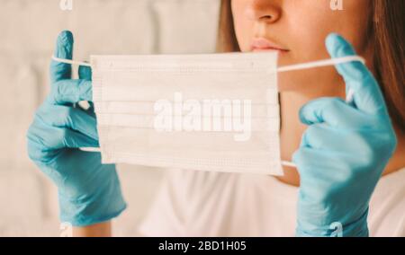 Closeup girl female doctor surgeon in protective gloves wears medical mask on face in hospital. Young confident woman putting on protective face mask. Stock Photo