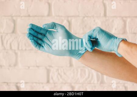 Closeup of man wearing blue latex medical gloves on hands. Professional doctor putting sterile protective gloves for patient examination in hospital. Stock Photo