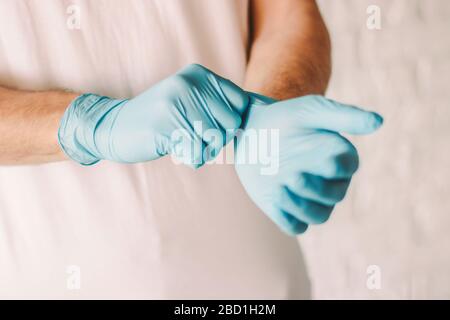 Closeup of professional doctor putting on blue latex gloves on hands. Man wearing sterile protective medical gloves on hands. Personal protection. Med Stock Photo