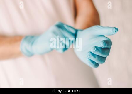 Closeup of man putting on medical protective gloves on hands. Professional doctor wearing sterile blue latex gloves on hands. Medical examination of c Stock Photo