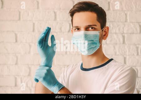 Confident man surgeon in medical mask on face wearing protective sterile glove on hand. Professional doctor in protective face mask putting on latex g Stock Photo