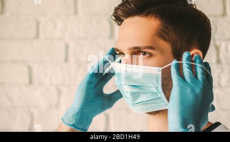 Young man in blue latex gloves putting on medical mask on face. Confident professional surgeon doctor in medical gloves on hands wearing protective fa Stock Photo