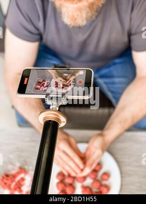 Man hands preparing meatballs with raw mincemeat recording video on smartphone. Lifestyle close up composition with natural light. Homemade cooking vl Stock Photo