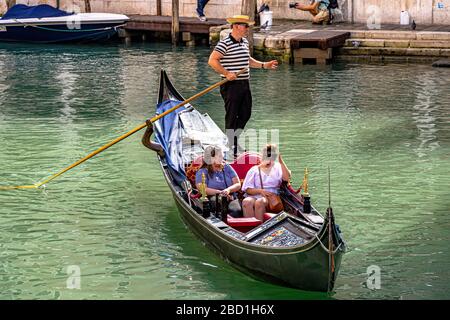 A Gondola in gondoliers uniform steers his gondola along a canal with two female tourists on-board, Venice ,Italy Stock Photo