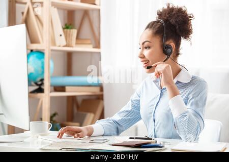 Tour agent in headset sitting at table in office talking with customer browsing computer joyful Stock Photo