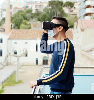 closeup of a caucasian man, wearing a surgical mask, using a virtual reality headset in a balcony Stock Photo