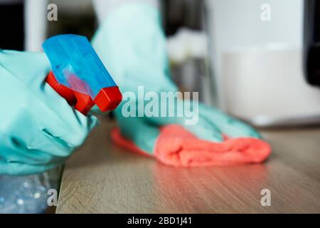 closeup of a man, wearing rubber gloves, cleaning the surface of a cupboard or a shelf with a dishcloth and a cleaner from a spray bottle Stock Photo