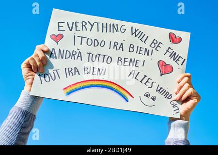 man showing a homemade sign with the text everything will be fine in different languages, such as Italian, German or French, as a message of hope duri Stock Photo