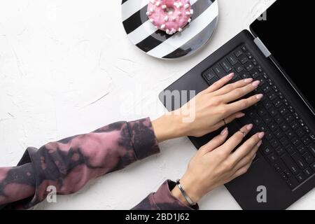 Manicured woman's hands in trendy pink hoodie typing on laptop. Stock Photo