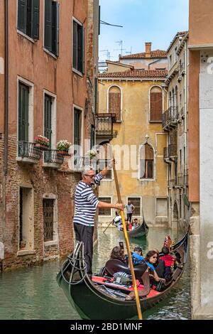 A gondola with tourists looking at the buildings as the Gondolier moves his gondola using his oar along Rio de San Moise ,a narrow canal in Venice Stock Photo