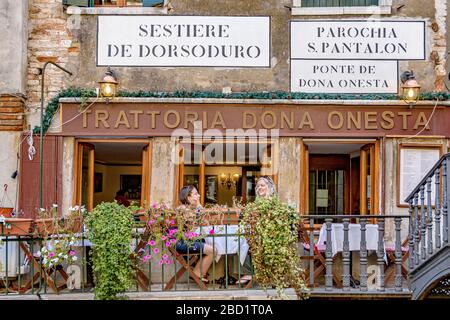 Two woman sitting at a table outside Trattoria Dona Onesta an Italian restaurant in the Dorsoduro district of Venice,Italy Stock Photo