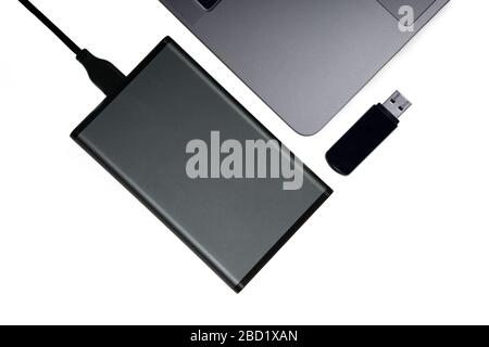 Portable hard disk connected to a laptop and a black flash drive isolated on white, flat lay. Data backup concept. Stock Photo