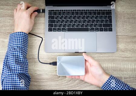 Man is connecting a portable hard drive to the laptop for data transfer or backup. Stock Photo